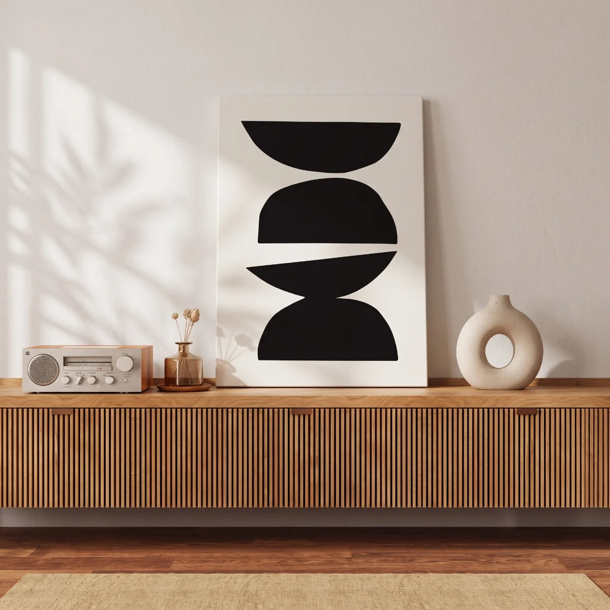 Cuadro abstracto de figuras geométricas negras apoyado en una credenza de madera en una sala moderna.