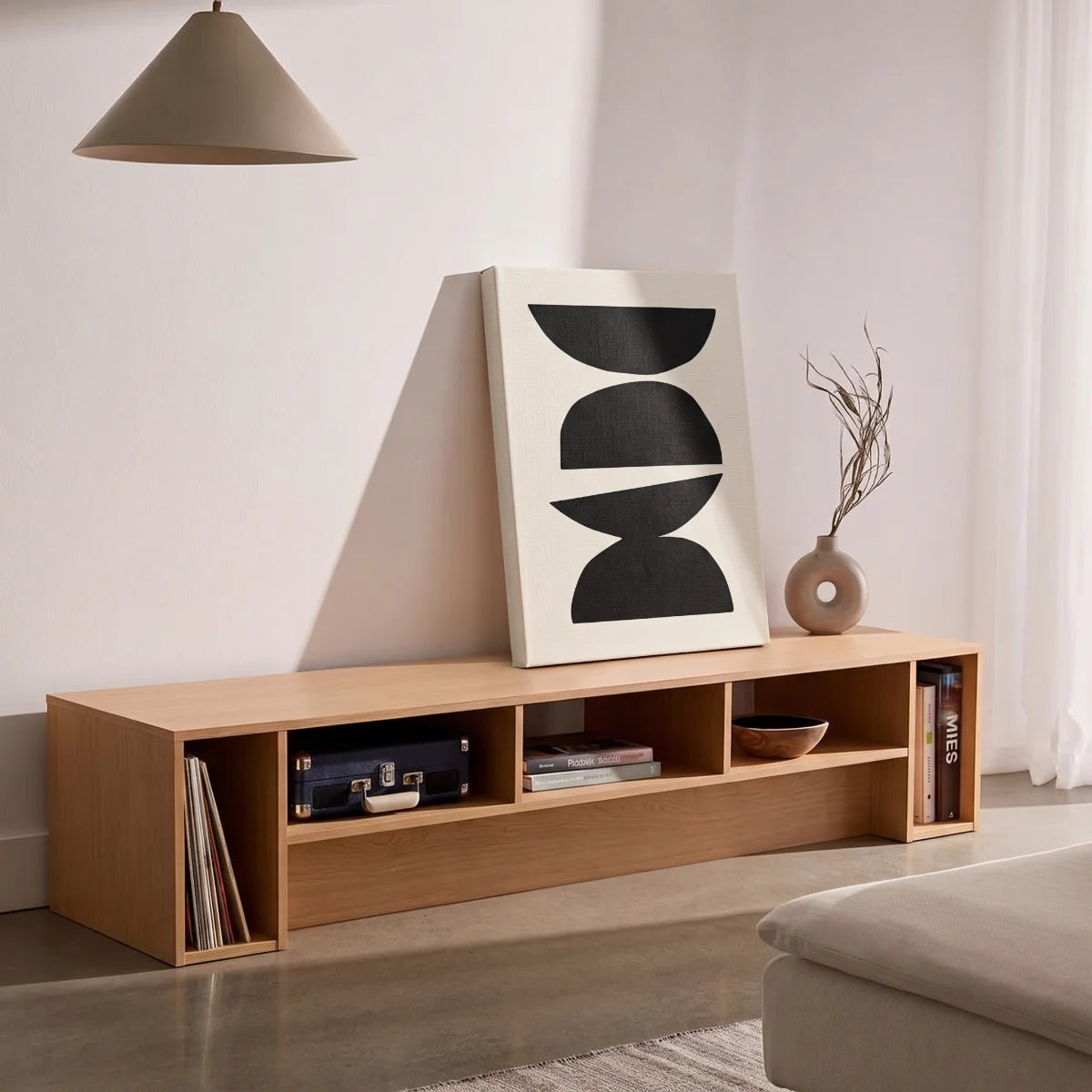 Cuadro en bastidor de arte Japandi apoyado en un mueble bajo de madera clara en un salón contemporáneo.
