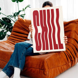 Mujer sentada en sofá moderno sosteniendo el cuadro decorativo CHILL frente a su rostro.