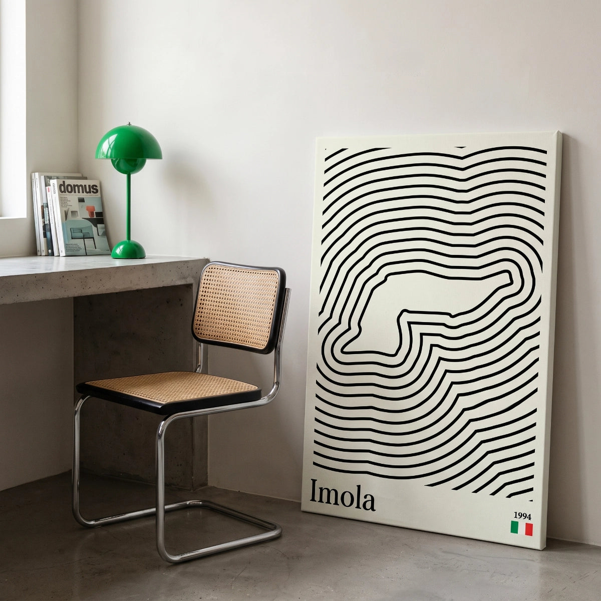 Cuadro en bastidor de gran formato de Imola F1 apoyado en el suelo junto a un escritorio en un estudio moderno.