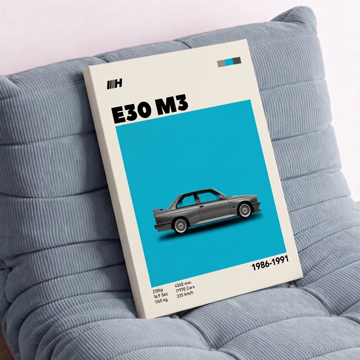 Cuadro de BMW M3 en bastidor apoyado sobre un sillón de diseño azul en una sala moderna.